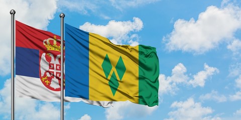 Serbia and Saint Vincent And The Grenadines flag waving in the wind against white cloudy blue sky...
