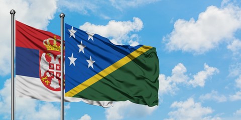 Serbia and Solomon Islands flag waving in the wind against white cloudy blue sky together. Diplomacy concept, international relations.