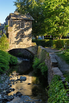 Bridge House on bridge over Stock Beck river with reflection of evening sunlight in Ambleside Lake District England