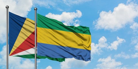 Seychelles and Gabon flag waving in the wind against white cloudy blue sky together. Diplomacy...