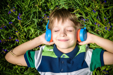 Smiling boy with arms under head lay under the sun on the green grass and listening music after school. Photo from above. Nature music relax concept