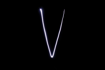 Alphabet made of neon light on a black background. Isolated top view, letter v.