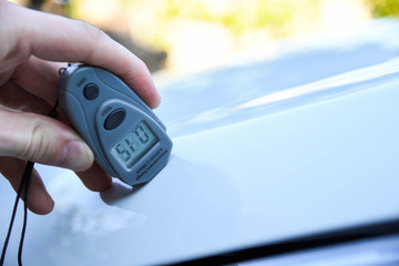 Male hand holds device for measuring coating thickness before polishing car. paint coating with...