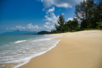 Waves of the azure Andaman sea under the blue sky reaching the shores of the sandy beautiful exotic and stunning Cenang beach in Langkawi island