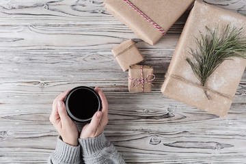 Female packing gifts. Cardboard box in craft paper, christmas rope and tree on the rustic wood planks background. DIY.
