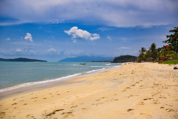 Waves of the azure Andaman sea under the blue sky reaching the shores of the sandy beautiful exotic and stunning Cenang beach in Langkawi island