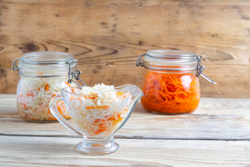  Spicy korean carrots and fermented cabbage in glass jars on a wooden table