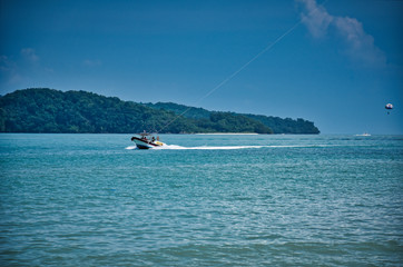Parasailing on the waves of the azure Andaman sea under the blue sky near the shores of the sandy beautiful exotic and stunning Cenang beach in Langkawi island,