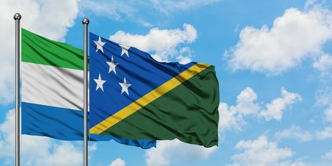 Sierra Leone and Solomon Islands flag waving in the wind against white cloudy blue sky together. Diplomacy concept, international relations.