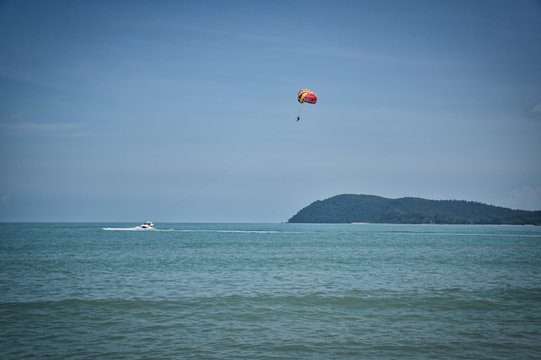 Parasailing on the waves of the azure Andaman sea under the blue sky near the shores of the sandy beautiful exotic and stunning Cenang beach in Langkawi island,
