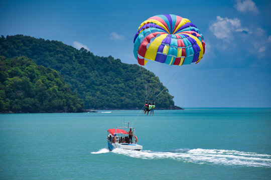 Parasailing on the waves of the azure Andaman sea under the blue sky near the shores of the sandy beautiful exotic and stunning Cenang beach in Langkawi island,