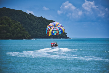 Parasailing on the waves of the azure Andaman sea under the blue sky near the shores of the sandy beautiful exotic and stunning Cenang beach in Langkawi island,