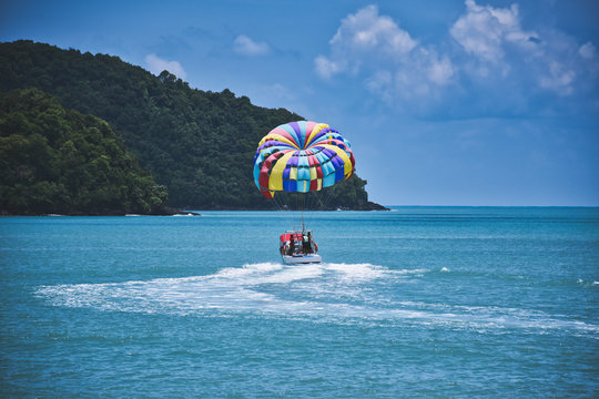 Parasailing on the waves of the azure Andaman sea under the blue sky near the shores of the sandy beautiful exotic and stunning Cenang beach in Langkawi island,