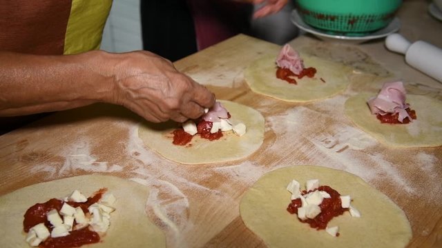 Feminine hands make Apulian panzerotti pies with tomato, mozzarella and prosciutto cotto. Panzerotti is a traditional dish in Salento, Puglia, Italy, fried in olive oil