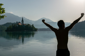 Fototapeta premium Silhouette of an European man doing morning healthy stretches, while bathing in lake Bled
