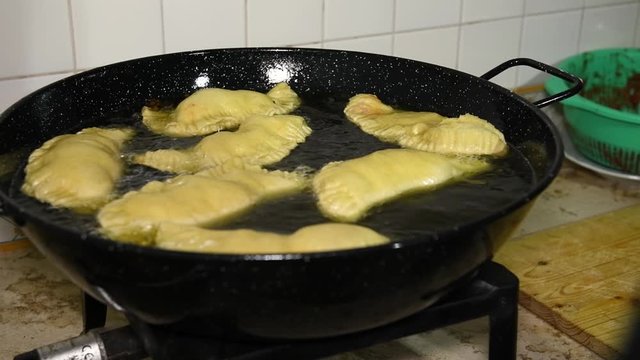 Frying Panzerotti. Female hands turn over apulian panzerotti patties, which are fried in olive oil in a large frying pan. Panzerotti is a traditional dish in Salento, Puglia, Italia