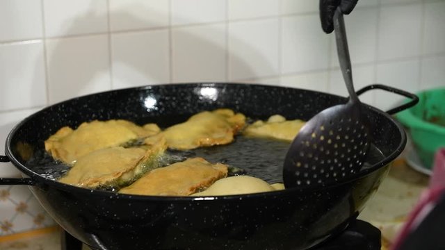 Frying Panzerotti. Female hands turn over apulian panzerotti patties, which are fried in olive oil in a large frying pan. Panzerotti is a traditional dish in Salento, Puglia, Italia