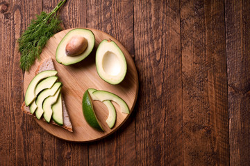 Beautifully plated avocado toast with delicious-looking toppings on wooden brouw background. Making sandwiches with avocado healthy organic food top view.On A Wooden Cutting Board Sliced avocado.