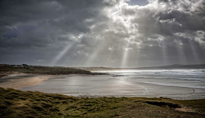 Rays of sunlight hitting stormy Cornish coastline with waves rolling in