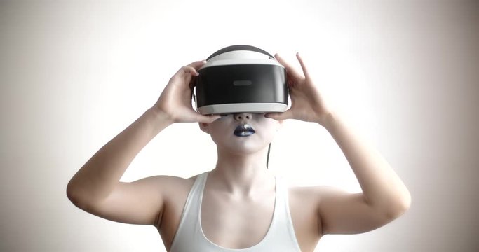 Young asian girl with bright artistic make-up wearing a vr helmet diving in world of vitual reality, moving her hands and interacting with it - technology concept closeup 4k footage