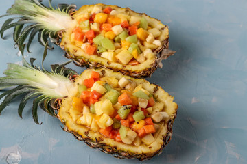 Tropical fruit salad in pineapple halves on a light blue background, horizontal orientation