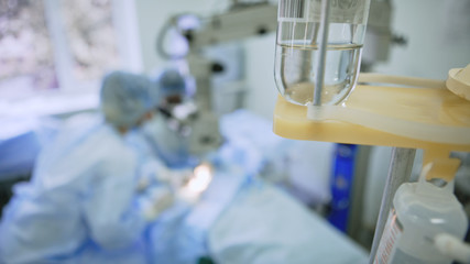 Team surgeons are performing an operation in a operating room, a drip in the foreground