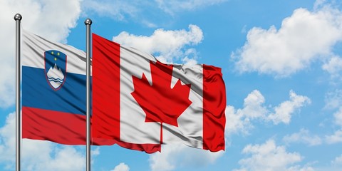 Slovenia and Canada flag waving in the wind against white cloudy blue sky together. Diplomacy concept, international relations.
