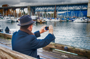 Dapper man photographs harbor with his cellphone while on vacation