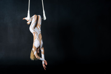 A young girl performs the acrobatic elements in the air trapeze. Studio shooting performances on a...