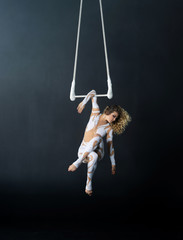A young girl performs the acrobatic elements in the air trapeze. Studio shooting performances on a black background