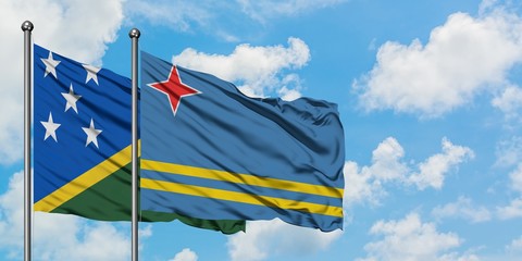 Solomon Islands and Aruba flag waving in the wind against white cloudy blue sky together. Diplomacy concept, international relations.