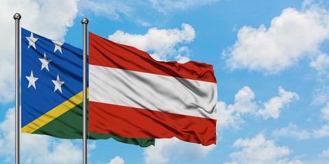 Solomon Islands and Austria flag waving in the wind against white cloudy blue sky together....