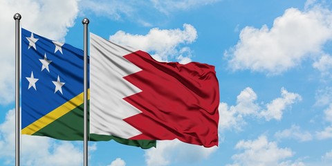 Solomon Islands and Bahrain flag waving in the wind against white cloudy blue sky together....
