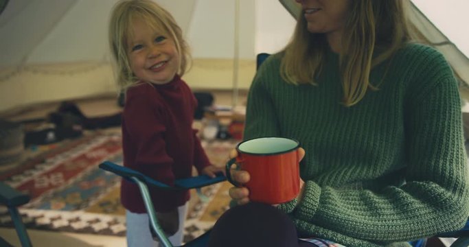 Young mother drinking coffee in tent with her toddler