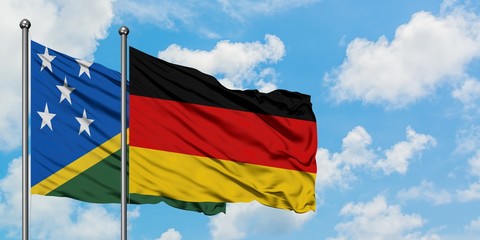 Solomon Islands and Germany flag waving in the wind against white cloudy blue sky together. Diplomacy concept, international relations.