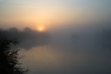 Moody atmosphere as the sun rises above a misty river
