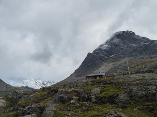wooden mountain hut cabin at massif Trolltindene, Troll wall Trollveggen, in Romsdal valley, Norway. Cloudy white sky clouds. Summer road trip travel scenery.