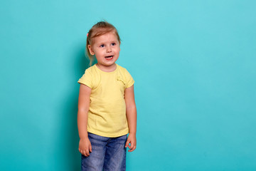 Close-up studio shot of a beautiful little girl. Little blonde girl in a yellow T-shirt on a blue background. The emotions of a child.