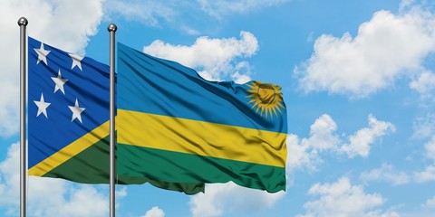 Solomon Islands and Rwanda flag waving in the wind against white cloudy blue sky together....