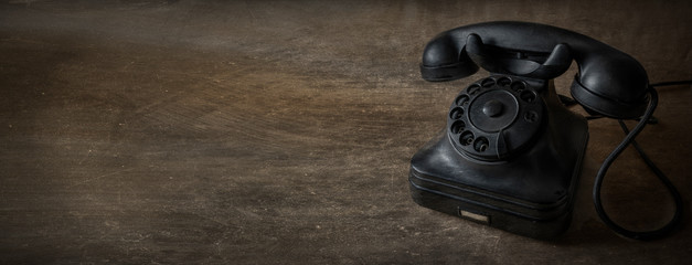 A black vintage dial telephone with woody background.