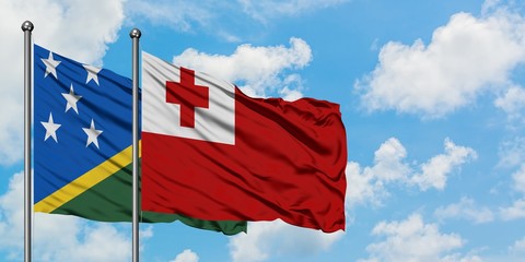 Solomon Islands and Tonga flag waving in the wind against white cloudy blue sky together. Diplomacy concept, international relations.