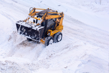 A small city excavator is used for local processing of city roads. Fighting heavy snow.