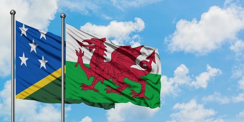 Solomon Islands and Wales flag waving in the wind against white cloudy blue sky together. Diplomacy...