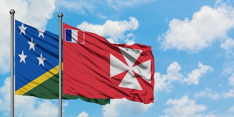 Solomon Islands and Wallis And Futuna flag waving in the wind against white cloudy blue sky together. Diplomacy concept, international relations.
