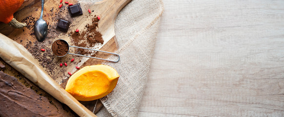 Ingredients for healthy cake with dark chocolate, pumpkin and cocoa. Baking in a pan on the wooden cutting board with copy space. Panoramic banner.