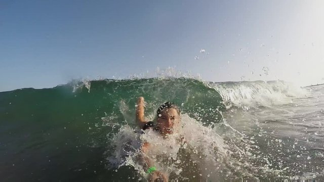 Boy with a monopod in his hands runs away from a rolling wave and dives into the water