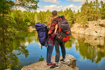 Couple of tourists exploring a new places. A handsome couple with backpack on nature near the lake at forest background.