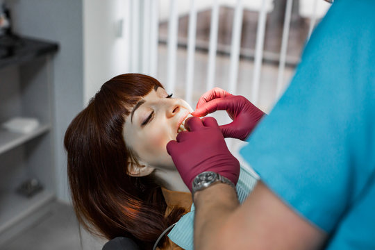 Cropped image of hands of the dentist in red medical gloves doing a dental treatment on a patient young girl