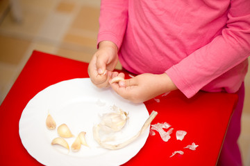 Obraz na płótnie Canvas Child peeling garlic on a plate
