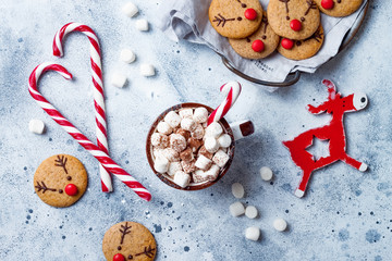 Hot cocoa with marshmallow in ceramic mug surrounded by Christmas gingerbread. Decorated red nosed...